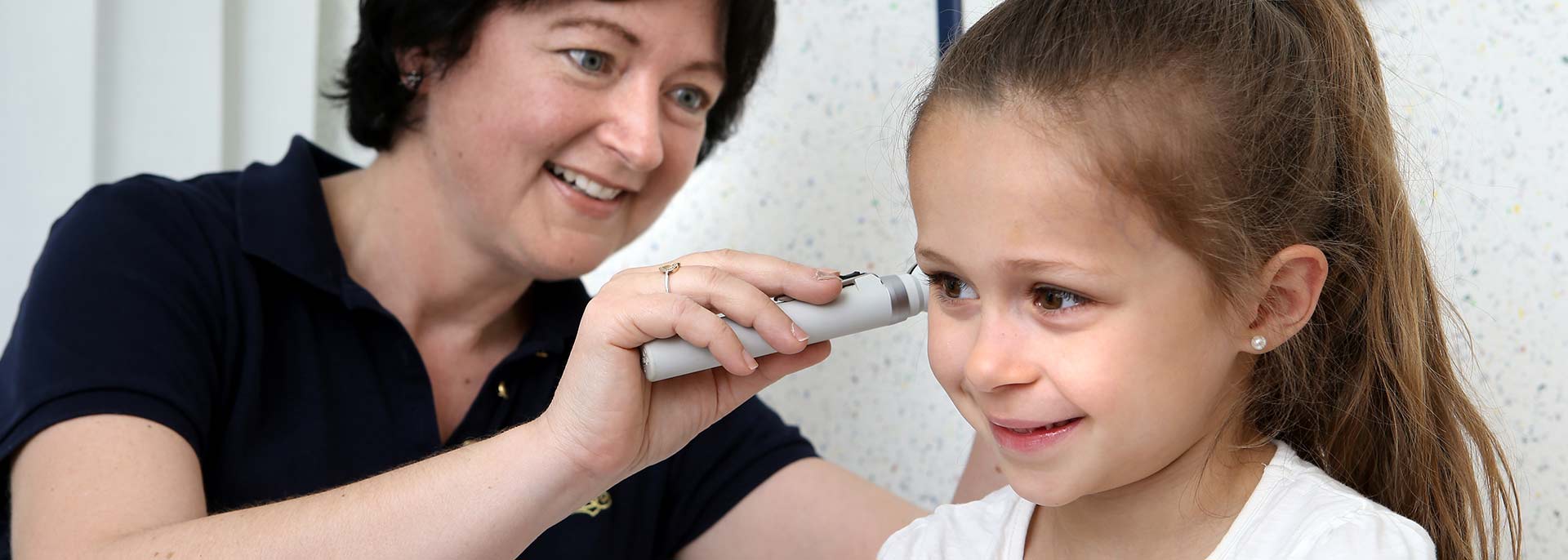Ärztin schaut Mädchen mit Ohrenspiegel ins Ohr 